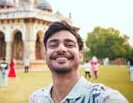 Young man takes a cheerful selfie at Humayun's Tomb, showcasing historic Mughal architecture.